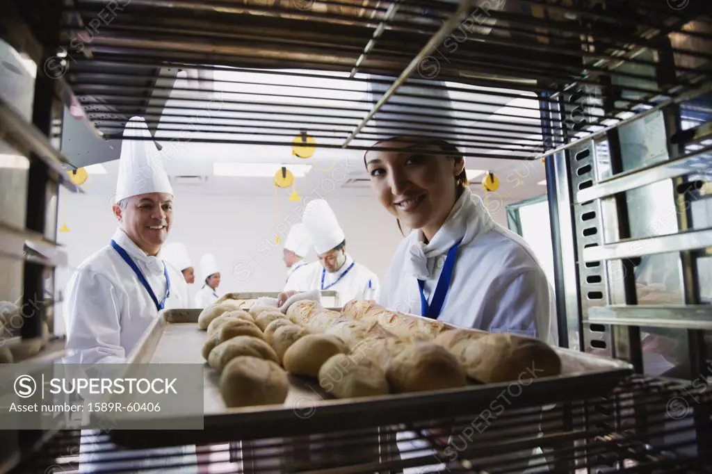 Asian female baker taking tray of bread off rack