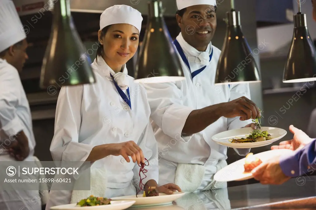 Multi-ethnic chefs garnishing plates of food