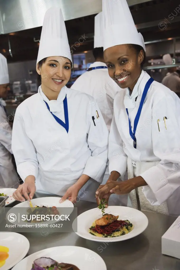 Multi-ethnic female chefs garnishing plates of food
