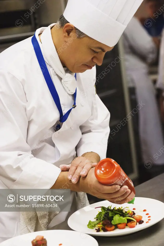Hispanic male chef garnishing plate of food