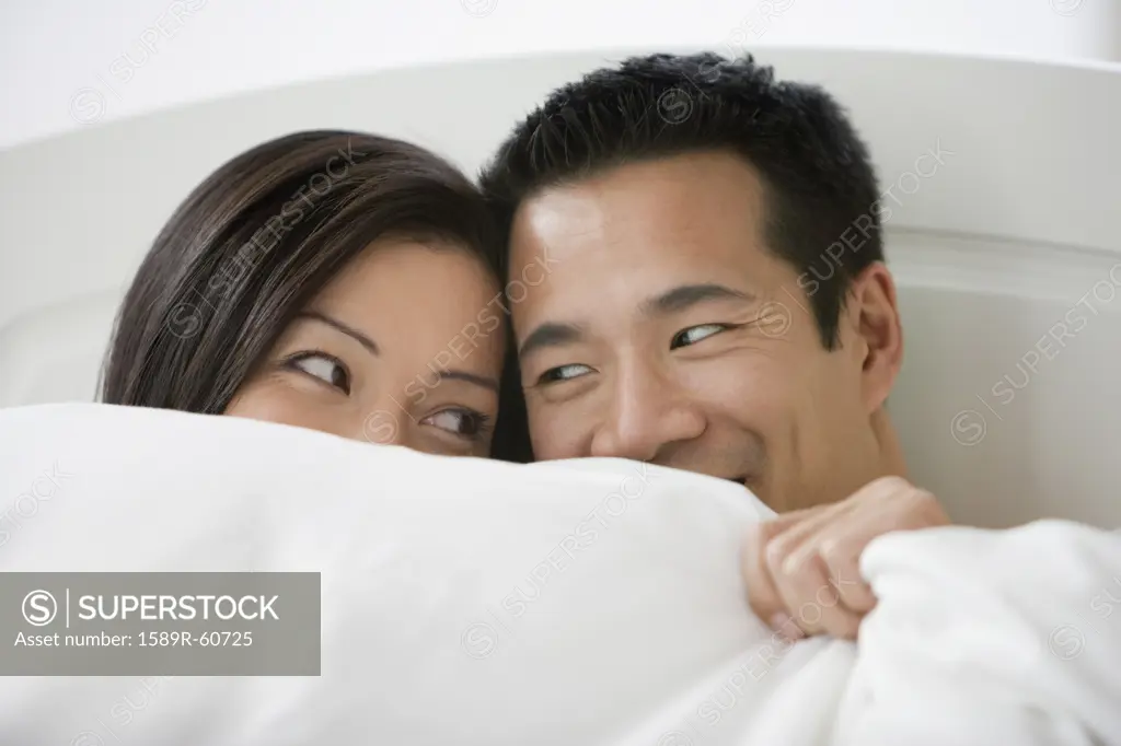 Asian couple smiling at each other in bed