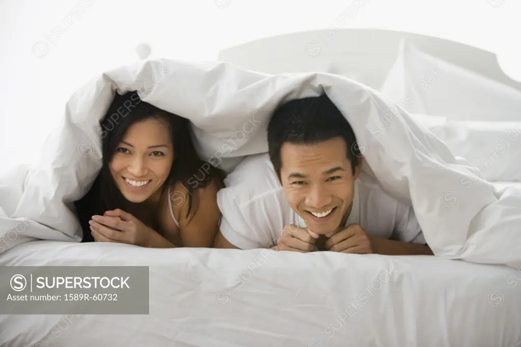 Asian couple laying under blanket