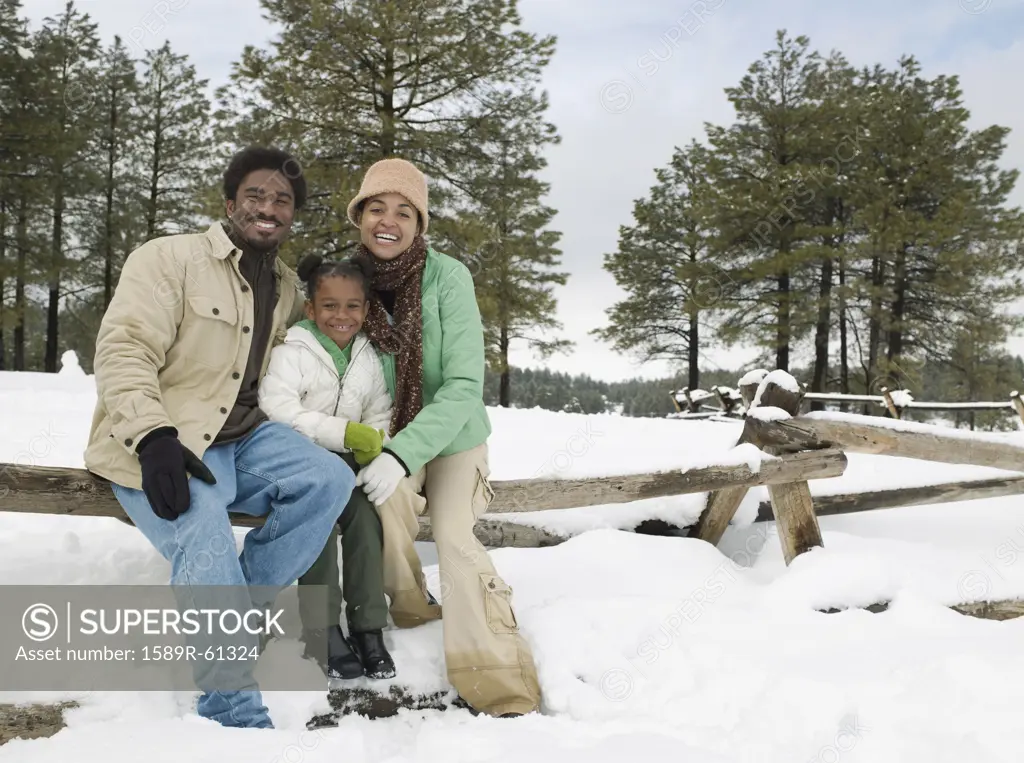 African family sitting on snowy wooden fence