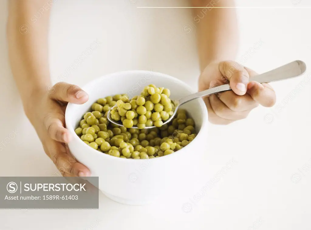 Close up of mixed race girl eating bowl of peas