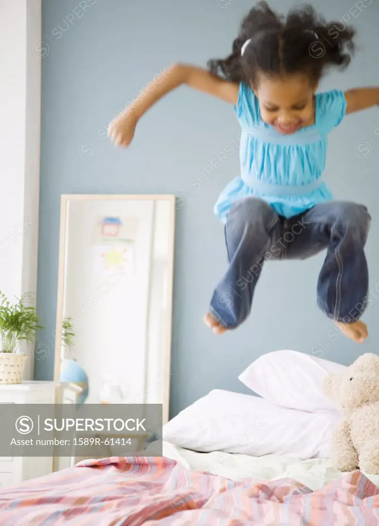 Mixed race girl jumping on bed
