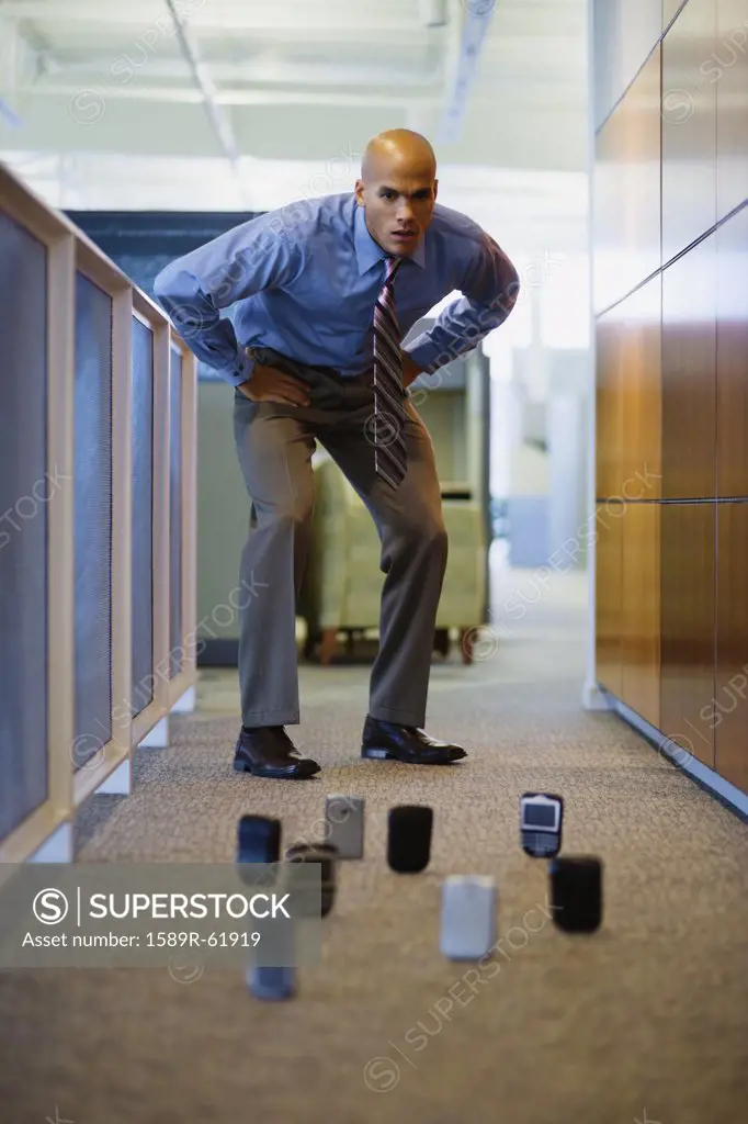 Mixed race man staring at cell phones on office floor