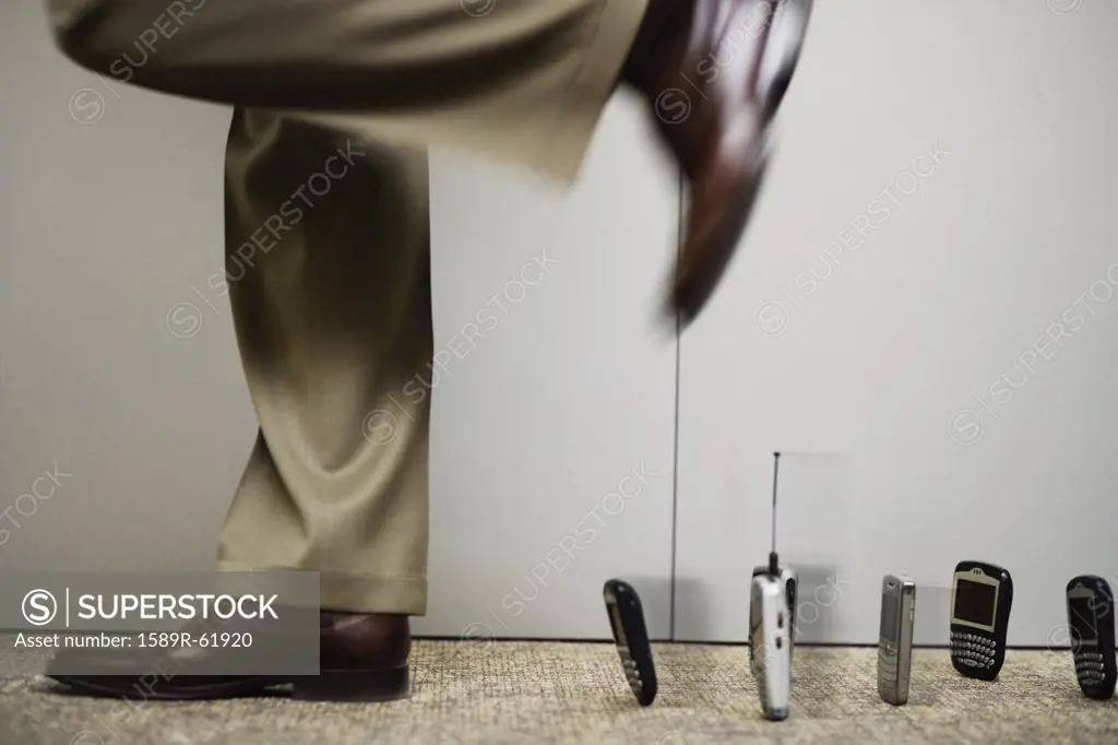 Mixed race businessman stepping over line of cell phones