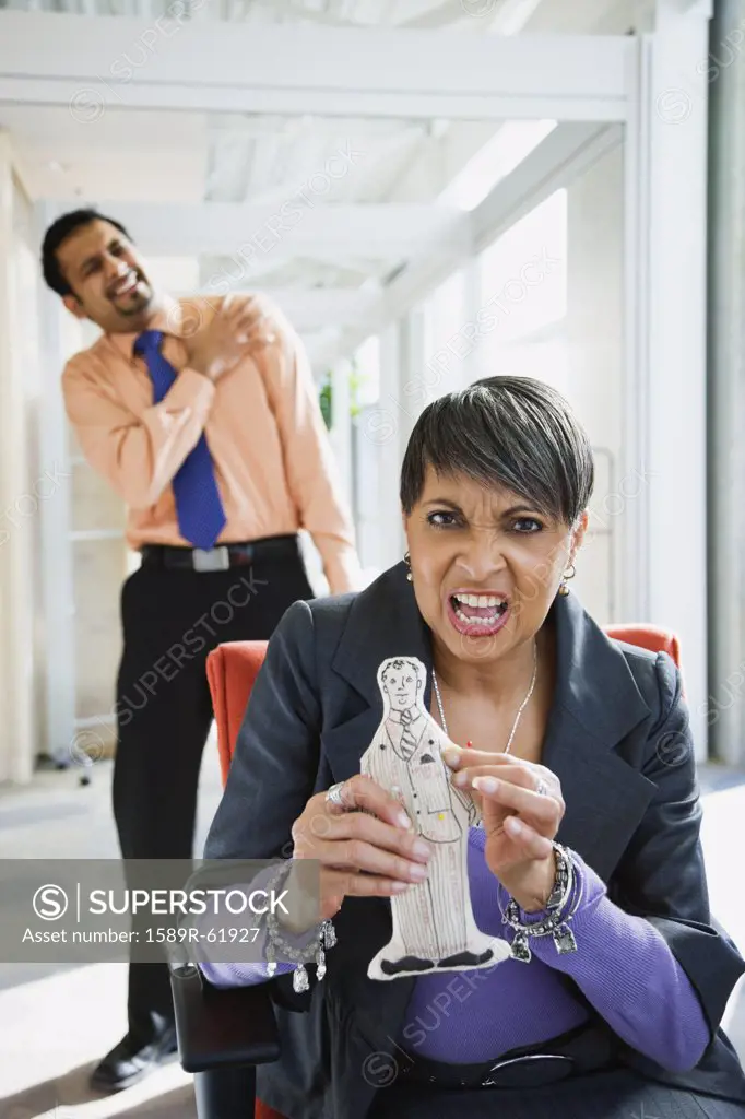 Angry African businesswoman holding voodoo doll of co-worker