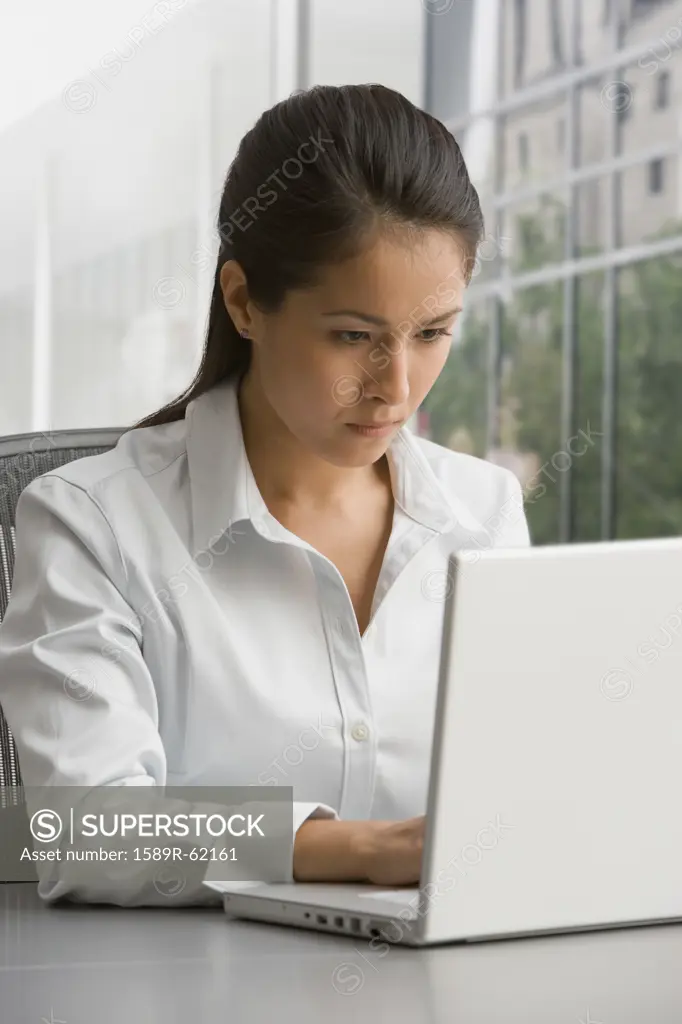 Eurasian businesswoman working on laptop