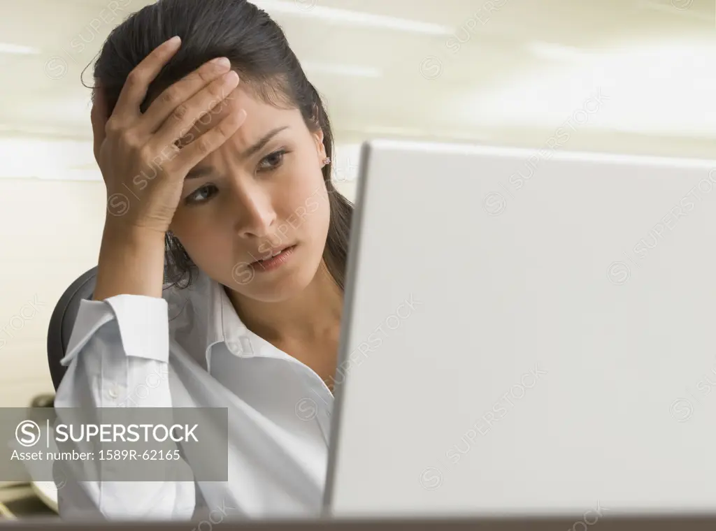 Eurasian businesswoman on laptop looking worried