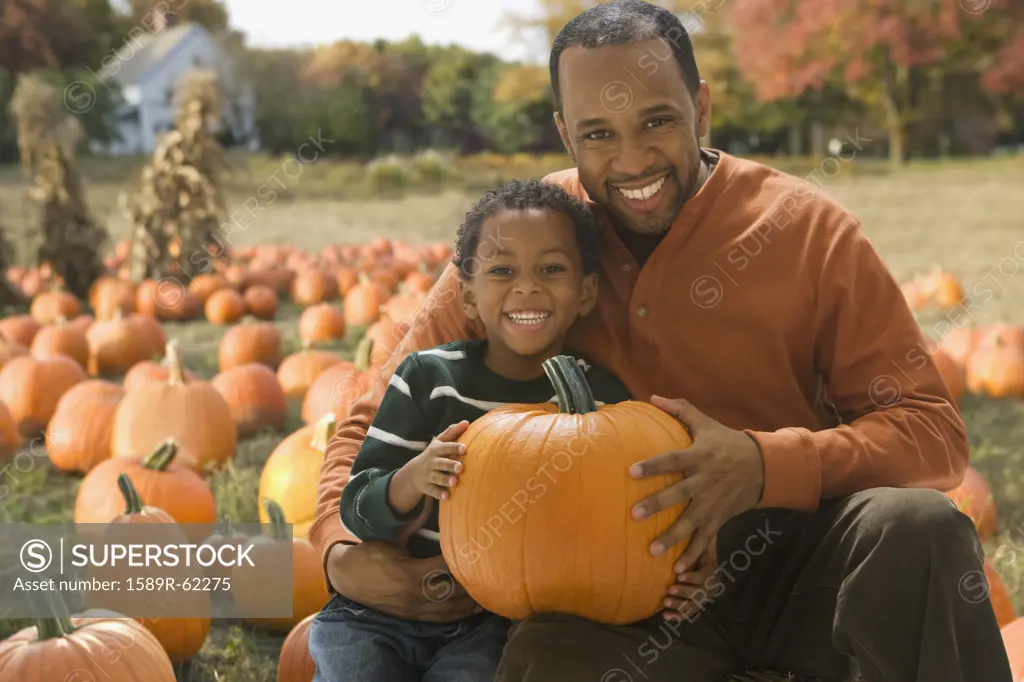 African father and son holding pumpkin at pumpkin patch
