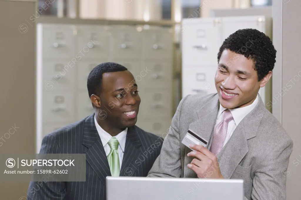 Multi-ethnic businessmen with laptop holding credit card