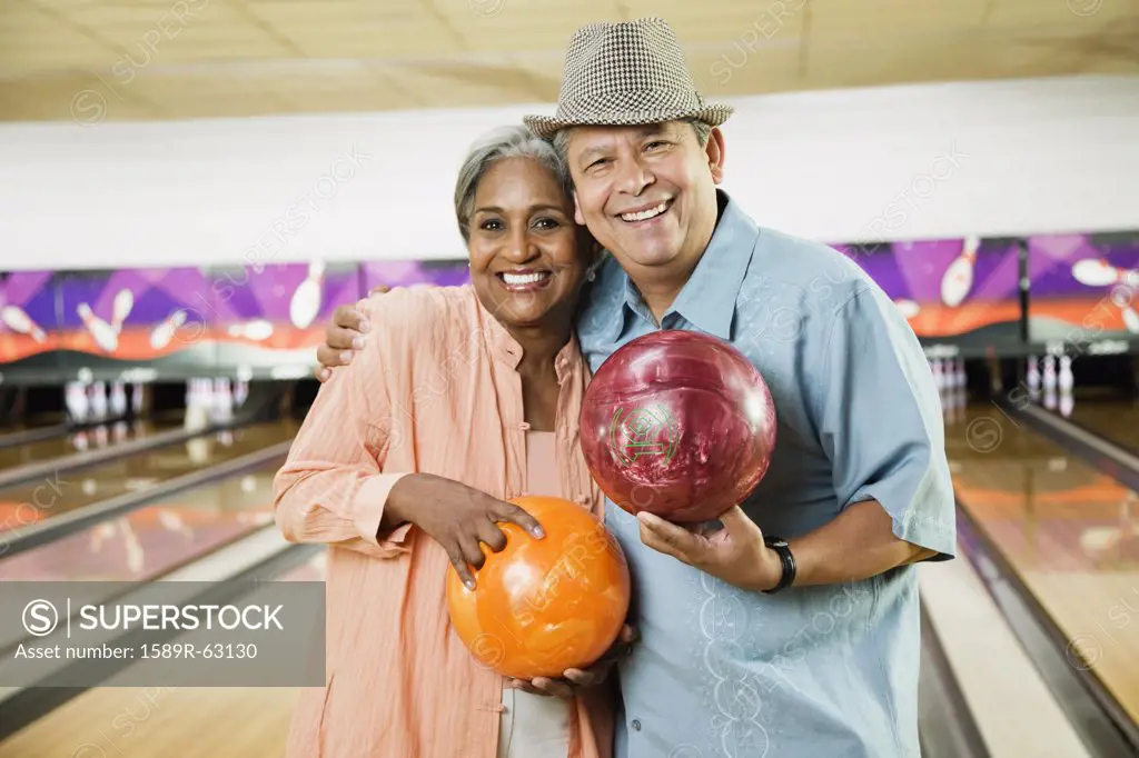 Multi-ethnic friends holding bowling balls in bowling alley