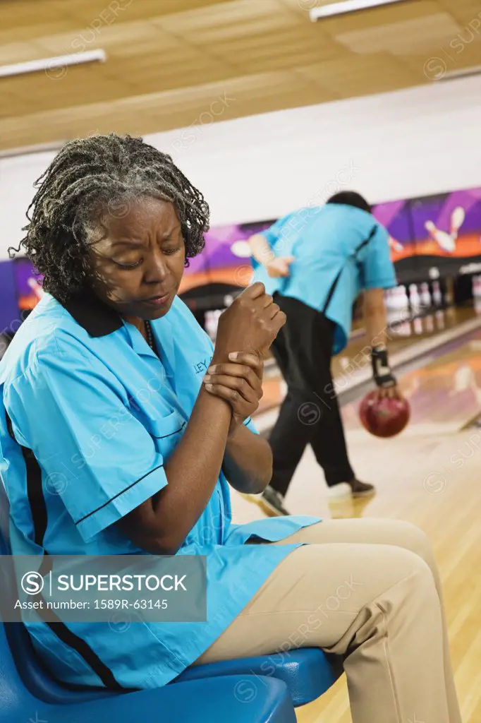 African woman rubbing aching wrist in bowling alley