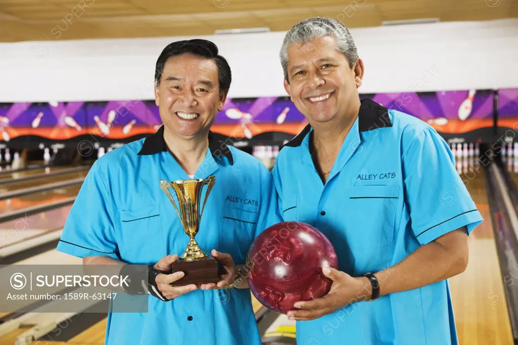 Multi-ethnic teammates holding bowling ball and trophy