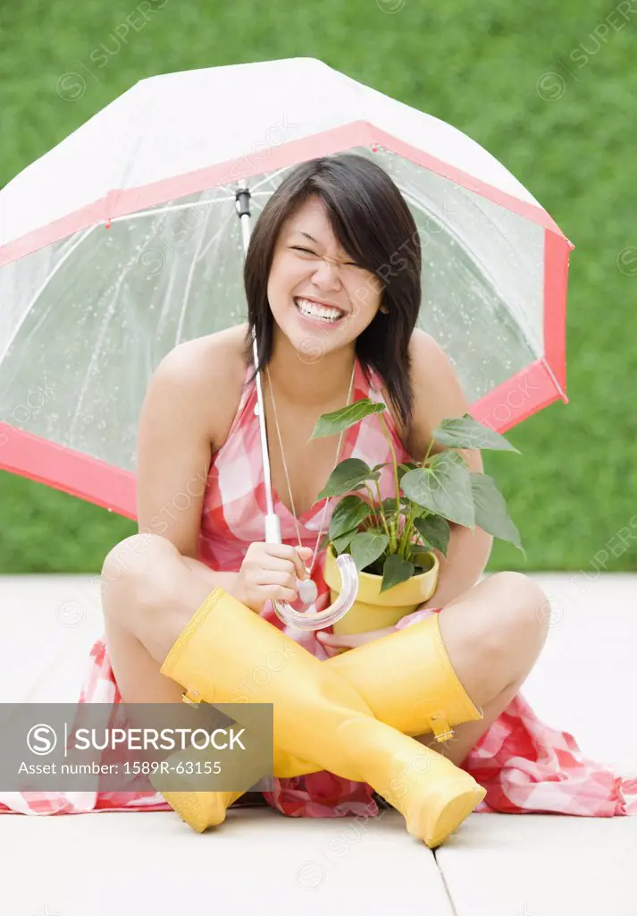 Asian woman sitting underneath umbrella in rain