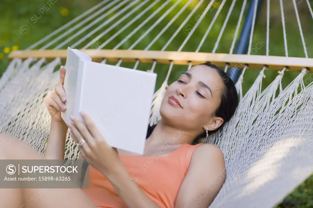 Hispanic woman laying in hammock reading