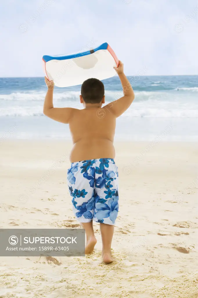 Hispanic boy carrying boogie board to ocean