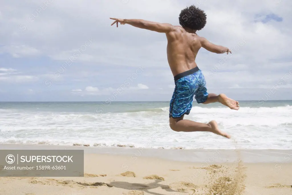 African man at beach jumping in mid-air