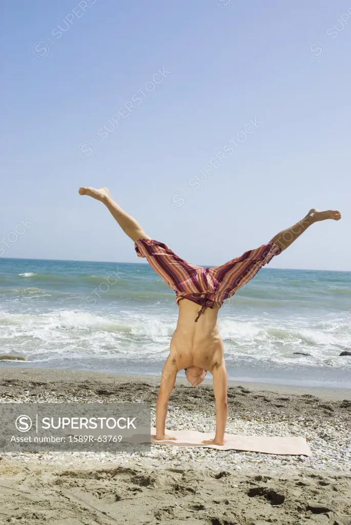 Hispanic man doing handstand on beach