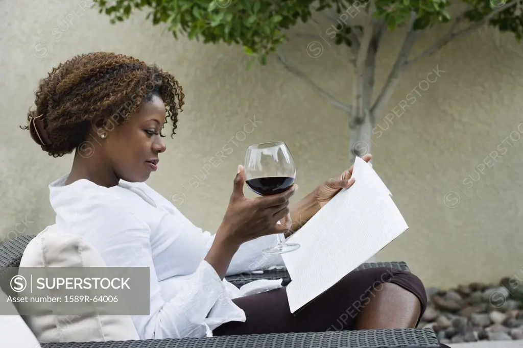African woman reading on patio and drinking red wine