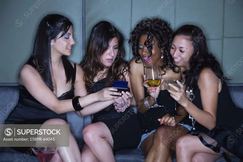 Women in nightclub drinking cocktails and text messaging on cell phone