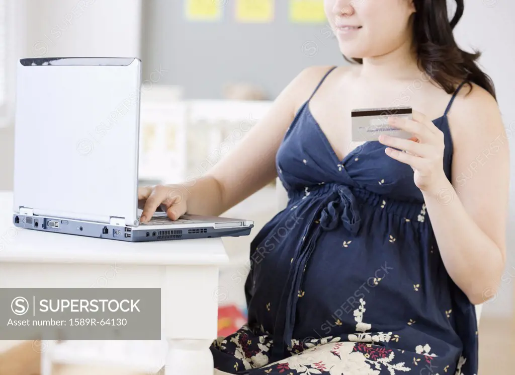 Pregnant Asian woman shopping online with credit card