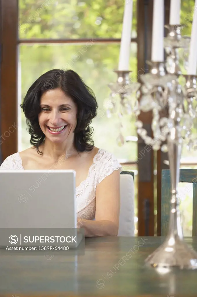 Confident Middle Eastern woman typing on laptop in dining room