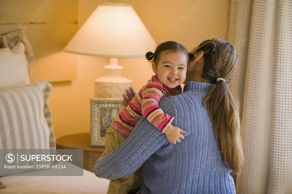 Hispanic mother and daughter hugging in bedroom