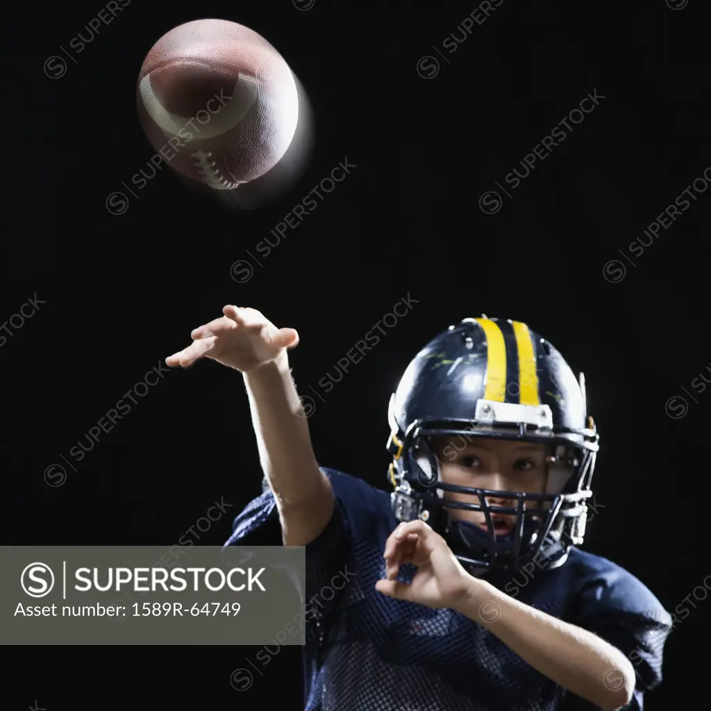 Hispanic boy in football uniform throwing ball