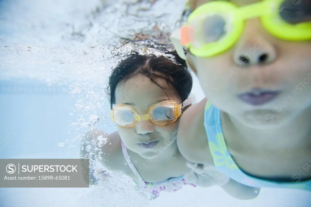 Hispanic girls swimming underwater in pool