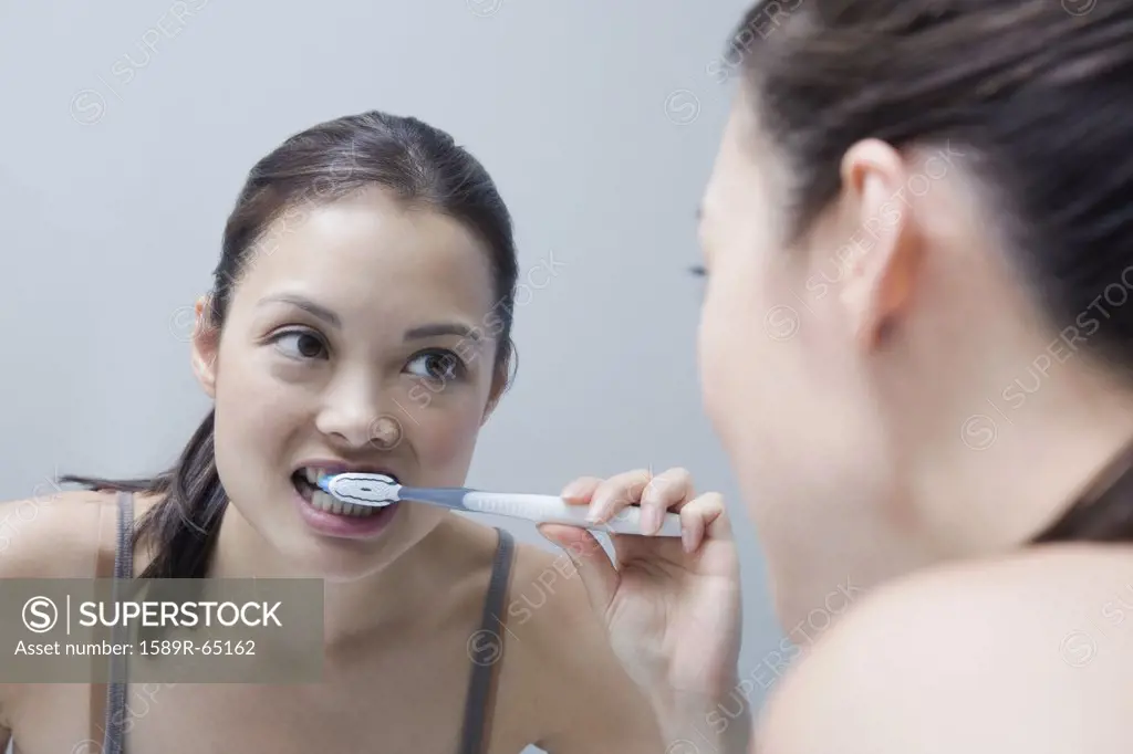 Woman brushing teeth in mirror