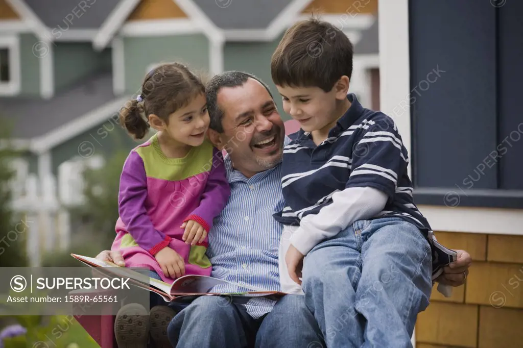 Father reading to son and daughter on porch