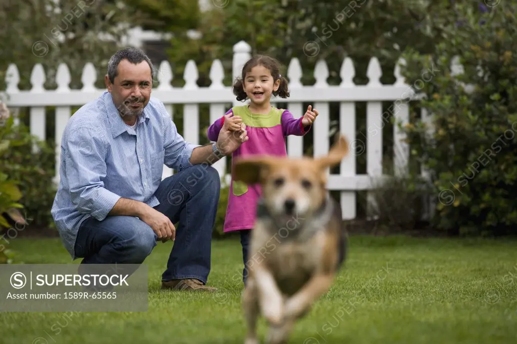 Father and daughter watching dog in backyard