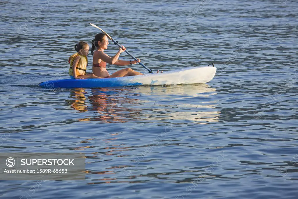 Mother and daughter rowing kayak on lake
