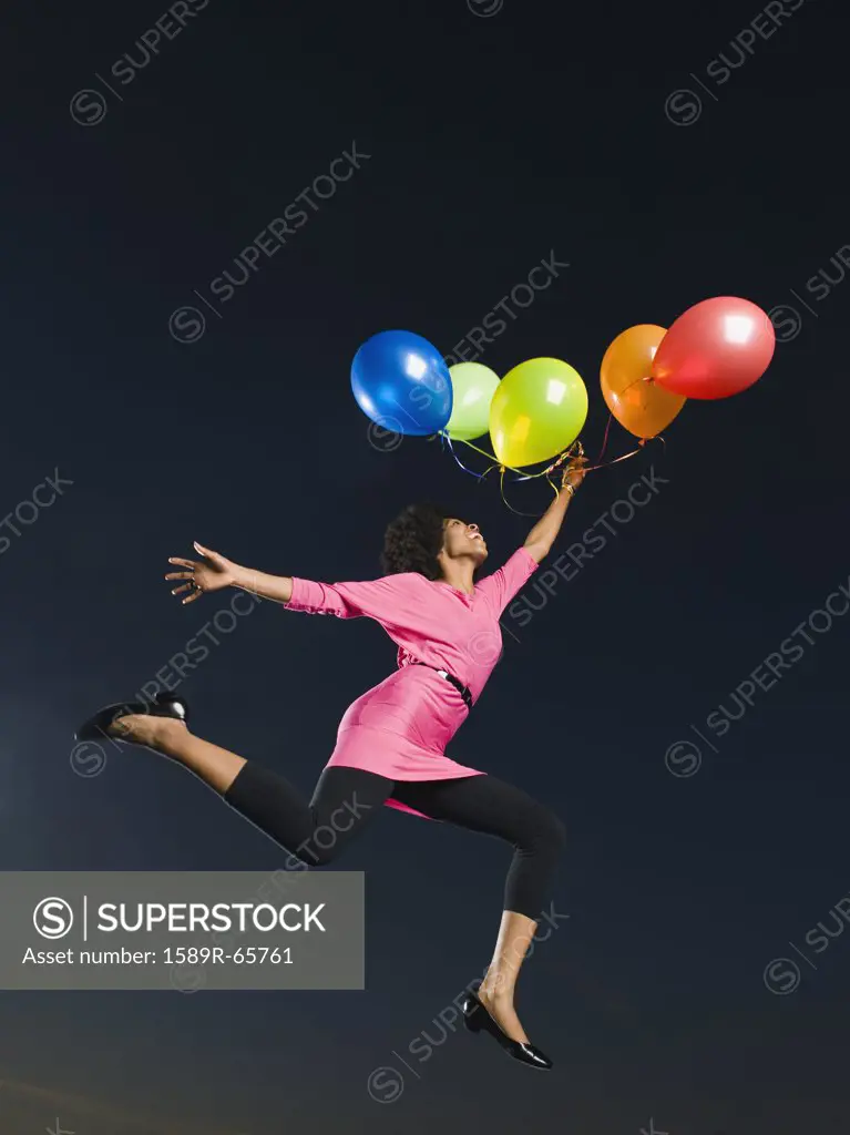 African woman holding bunch of balloons in mid-air