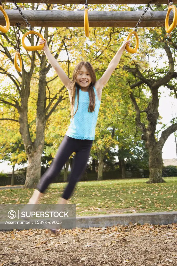 Mixed race young girl swinging from playground equipment