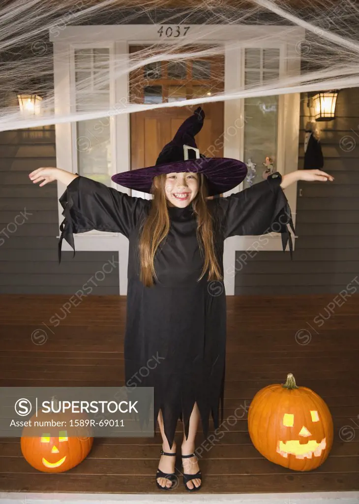 Mixed race young girl in witch costume with Halloween pumpkins