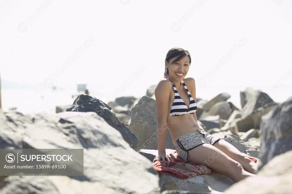 Asian woman wearing bikini sitting on rocks