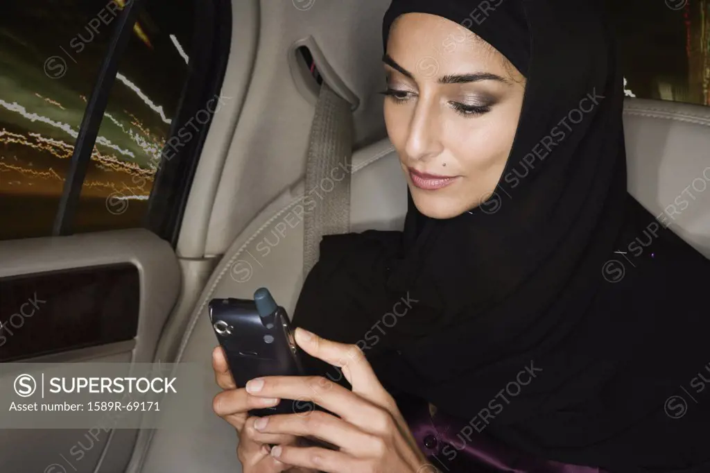 Middle Eastern woman using cell phone in car