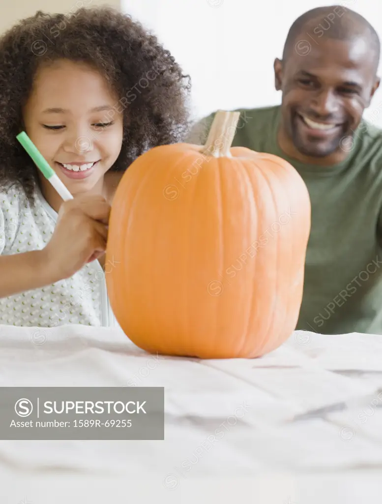 African father and daughter drawing on pumpkin