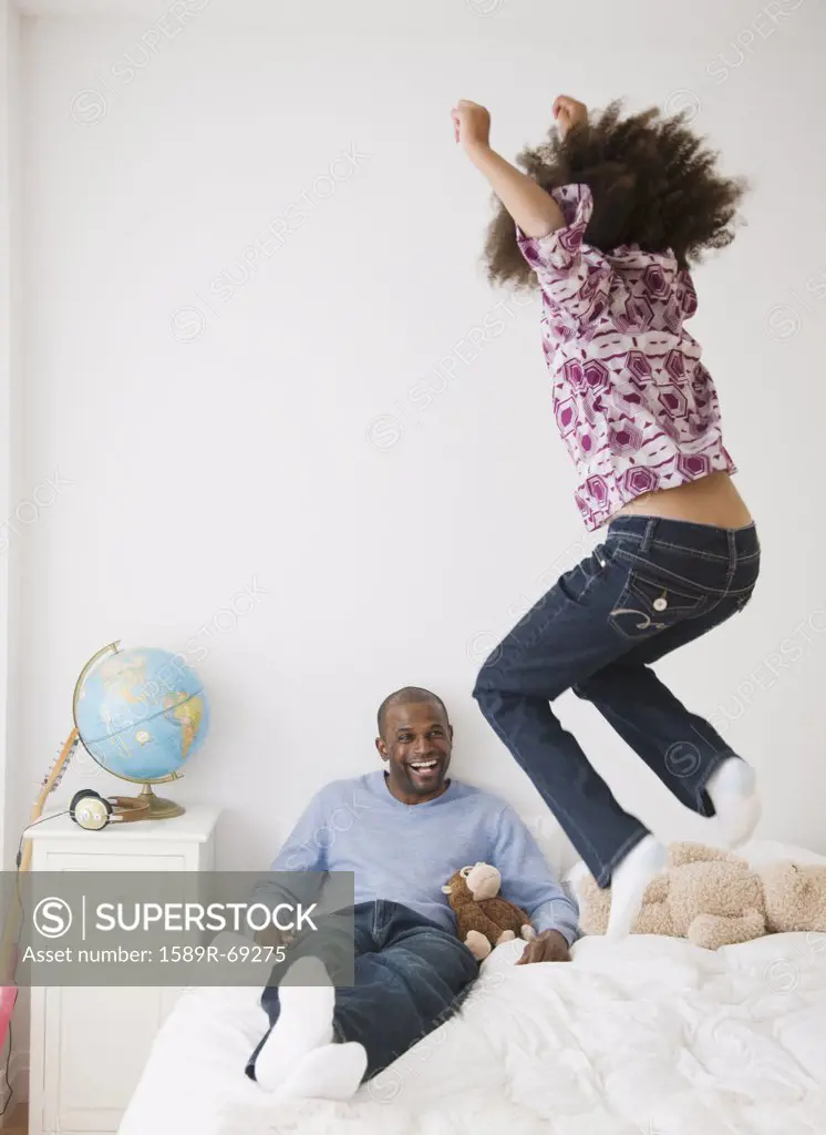 African father and daughter playing on bed