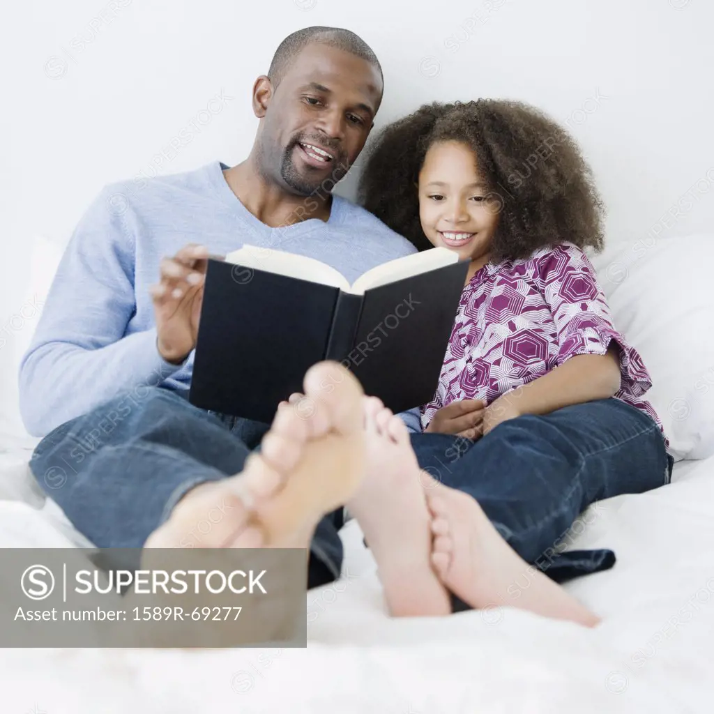 African father reading to daughter on bed
