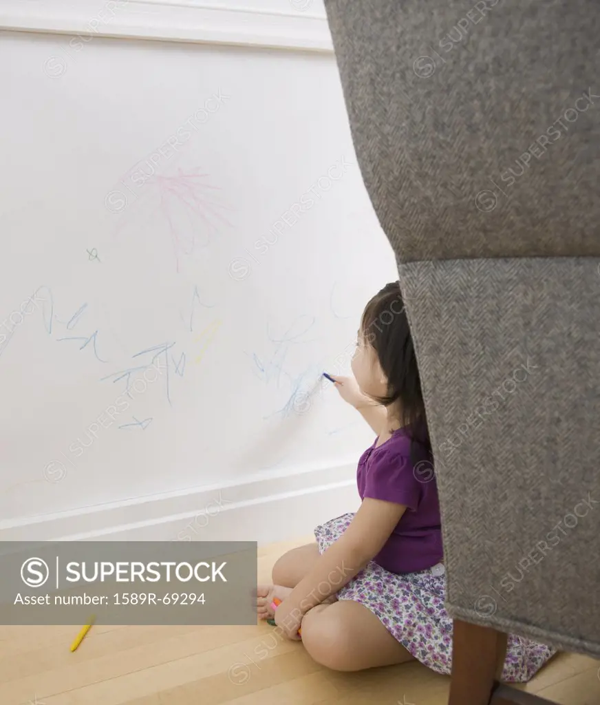 Toddler girl drawing on wall with crayons