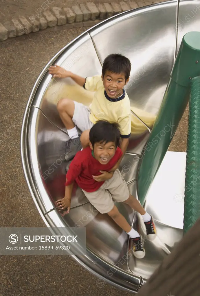 Asian boys sliding down circular slide