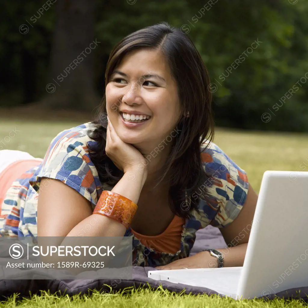 Asian woman laying in park with laptop