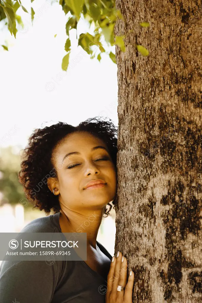 African woman leaning against tree with eyes closed