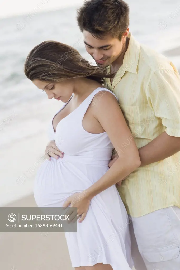 Husband hugging pregnant wife on beach