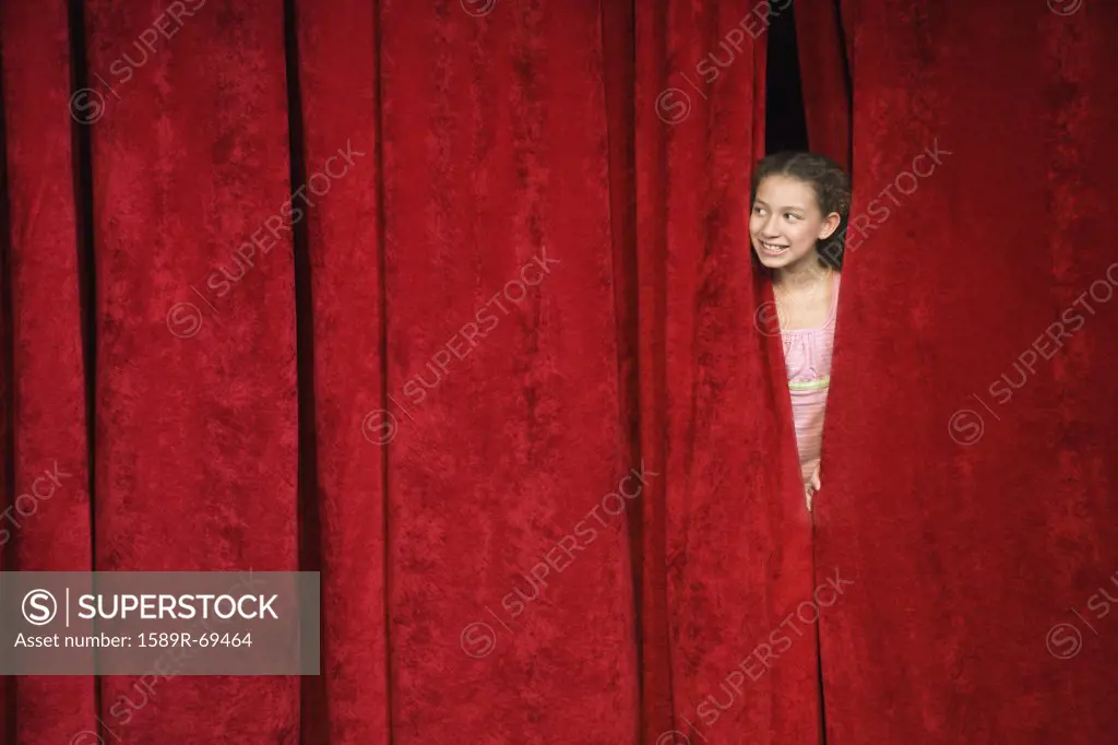 Mixed race person hiding behind stage curtain