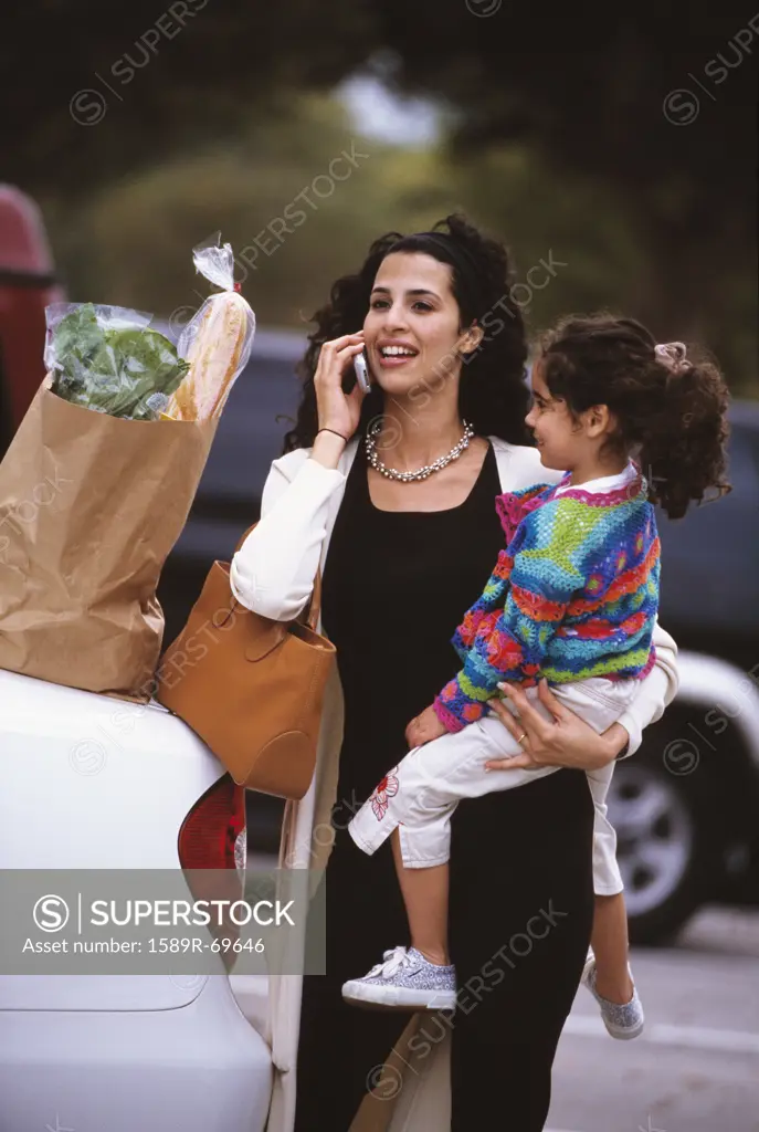 Hispanic mother talking on cell phone and holding daughter